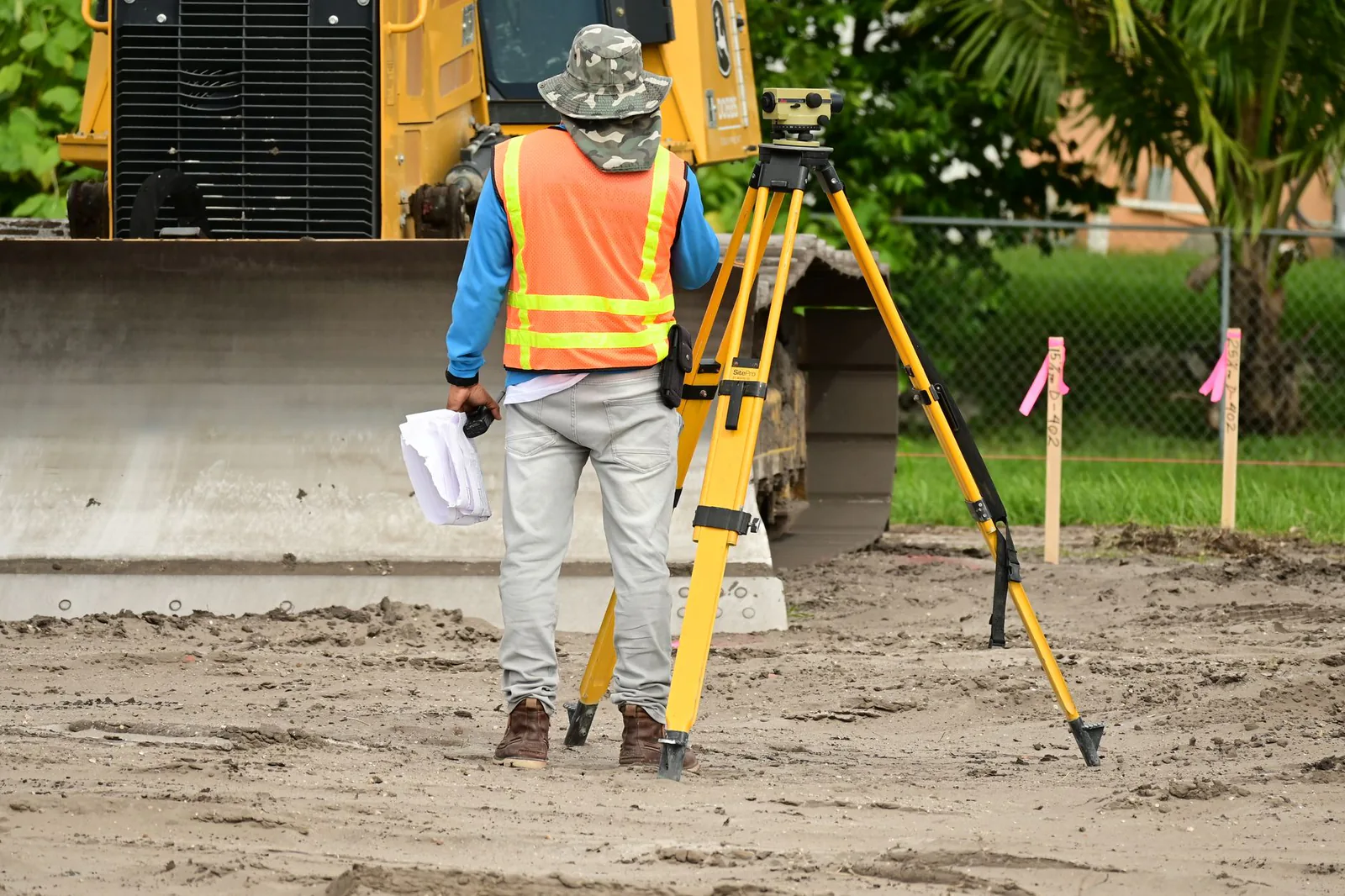 Land surveyor taking a reading with a tripod-mounted level near survey stakes