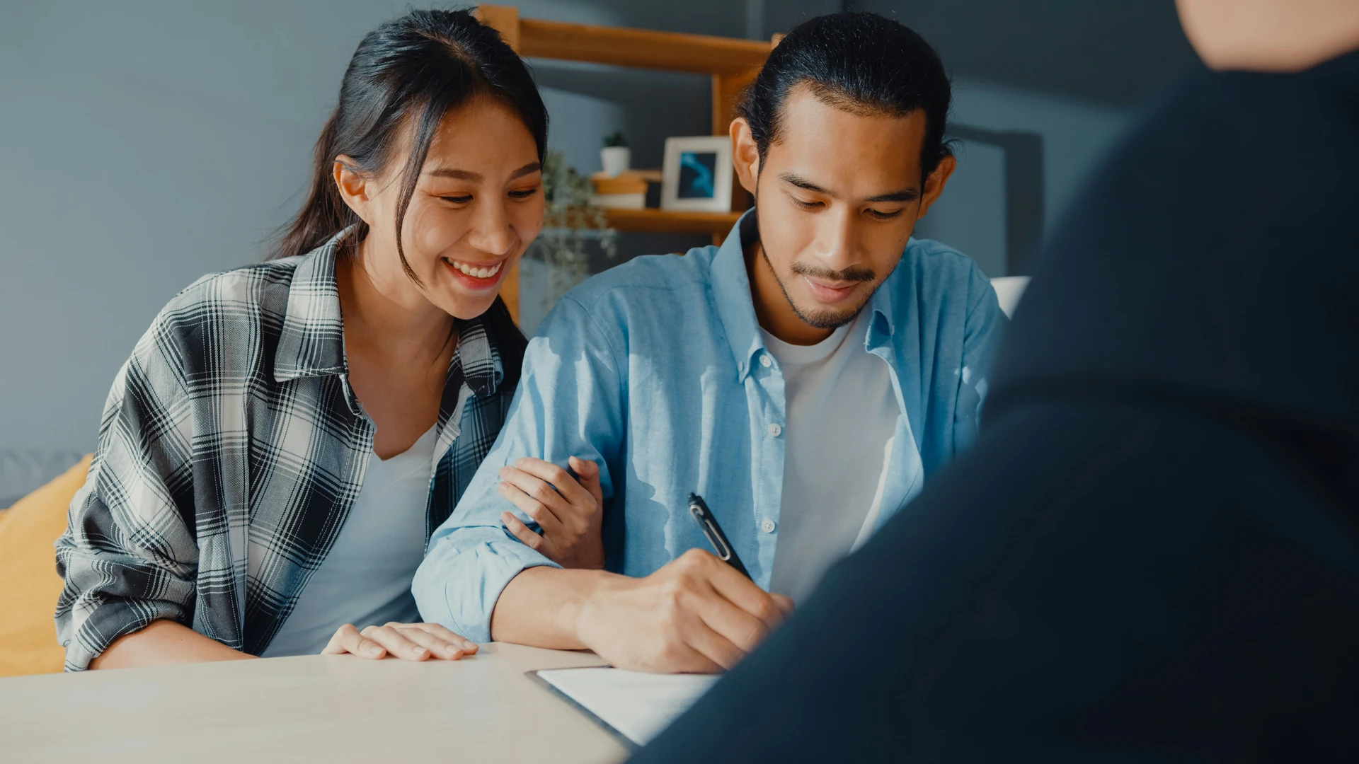 Couple souriant signant un document lors d'une rencontre avec son courtier immobilier.