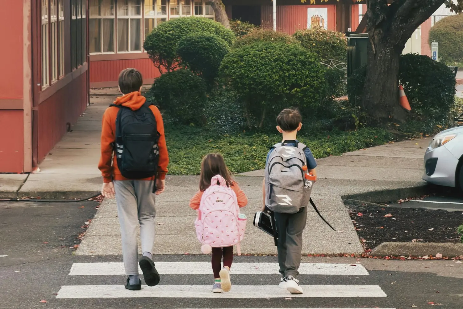 Three children with backpacks crossing the street to school, a key factor when choosing a family neighbourhood in Saint-Jérôme