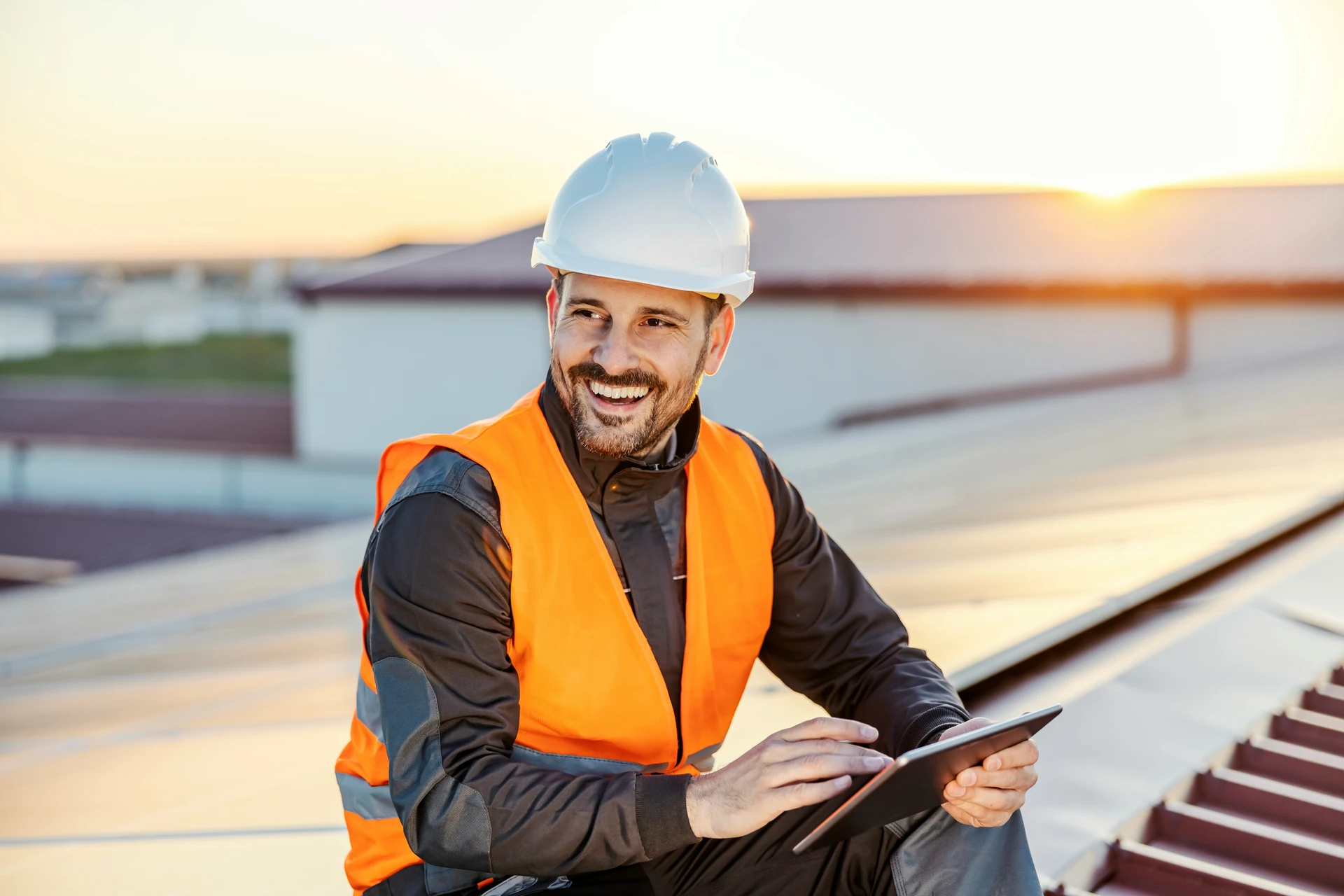 Building inspector smiling on a roof, tablet in hand, during an inspection