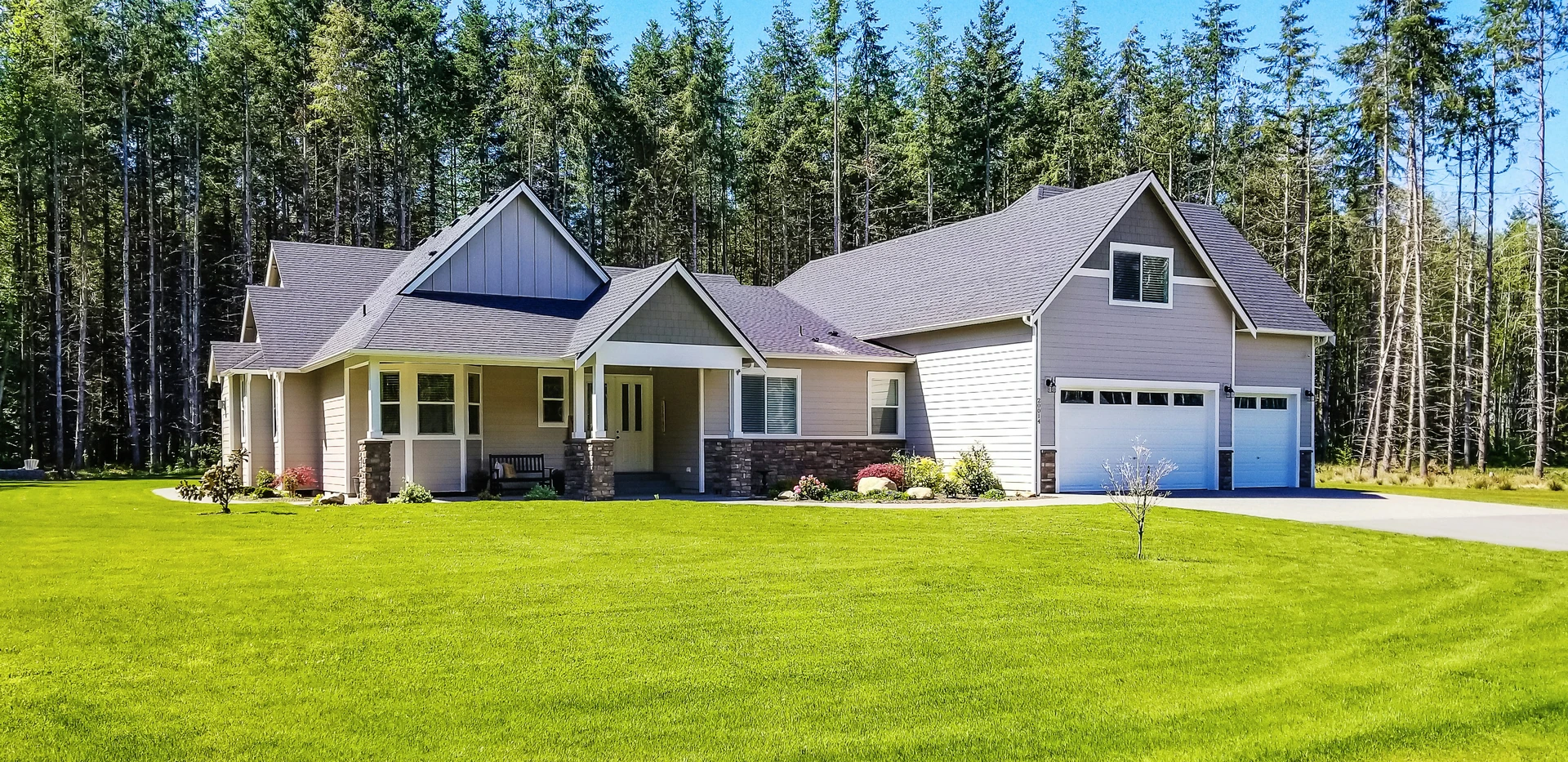 Large single-family home with a double garage and a wide lawned lot bordered by conifers