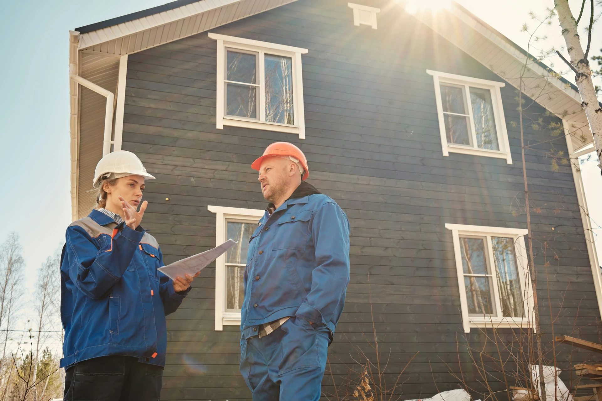 Two hard-hatted professionals discussing a report in front of a wood-clad house