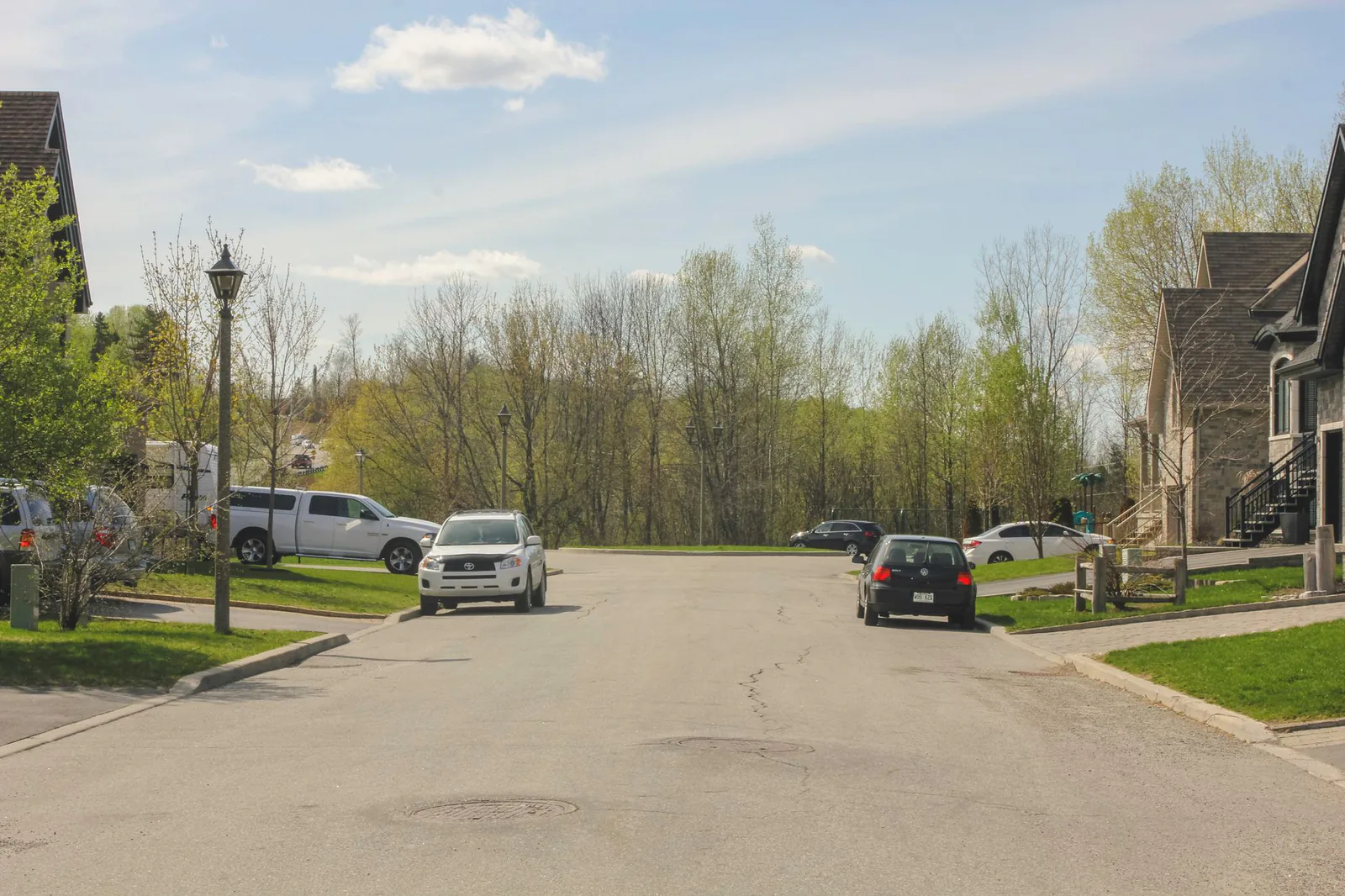 Residential street lined with single-family homes and parked cars in spring